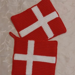 Könnte beinhalten: Zwei rote und weiße gehäkelte Topflappen mit dänischer Flaggen-Optik.