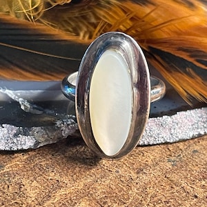 May include: A silver ring with an oval-shaped mother-of-pearl stone set in a silver bezel.