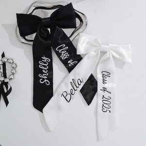 May include: Two black and white satin hair bows with personalised names and the text "Class of 2025".