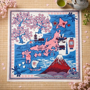 May include: Square cotton hand towel with a map of Japan in pink and blue. The map includes illustrations of landmarks, cherry blossoms, and a sailboat. The towel has a white border with pink floral accents.