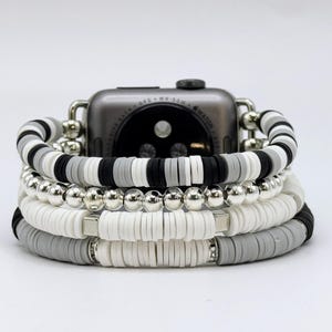 May include: A black and white beaded Apple Watch band with a silver metal accent. The band is made of stacked layers of round beads and flat, round beads.