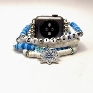 May include: A white and blue beaded Apple Watch band with a snowflake charm and the words "Let It Snow" spelled out in white beads.