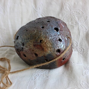 K&ouml;nnte beinhalten: Ein brauner, grauer und goldener Keramik-H&auml;ngepflanztopf mit einem Seilgriff. Der Topf hat eine raue, strukturierte Oberfl&auml;che und ist mit kleinen L&ouml;chern verziert.