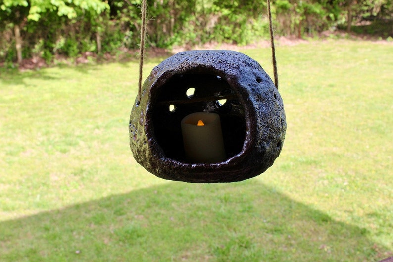 K&ouml;nnte beinhalten: Eine dunkelbraune, h&auml;ngende Keramiklaterne mit einer Kerze im Inneren. Die Laterne hat eine raue, strukturierte Oberfl&auml;che und h&auml;ngt an einer Schnur.