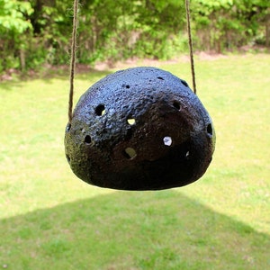 K&ouml;nnte beinhalten: Ein schwarzer Keramik-H&auml;ngepflanztopf mit einer strukturierten Oberfl&auml;che und mehreren L&ouml;chern. Der Topf h&auml;ngt an einer Schnur.