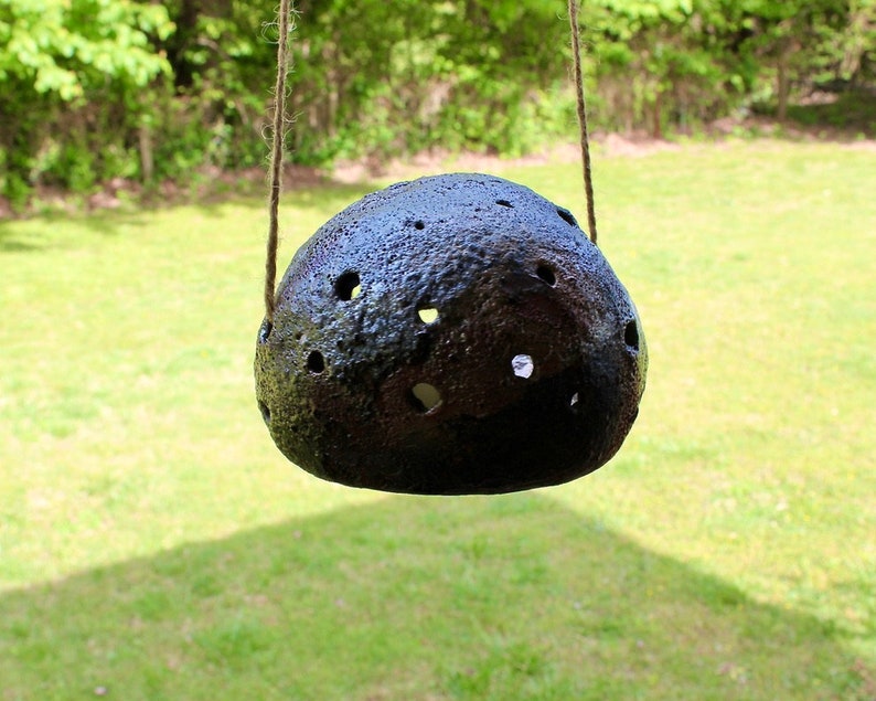 K&ouml;nnte beinhalten: Ein schwarzer Keramik-H&auml;ngepflanztopf mit einer strukturierten Oberfl&auml;che und mehreren L&ouml;chern. Der Topf h&auml;ngt an einer Schnur.