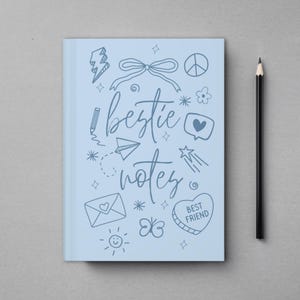 May include: A light blue notebook with the words "bestie notes" in cursive, surrounded by doodles. A black pencil rests beside the notebook on a gray surface. The notebook features a heart-shaped design that says "Best Friend".