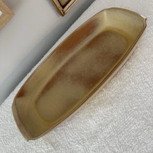 Puede incluir: Una fuente rectangular de cerámica en tonos marrón claro y beige. La fuente tiene un borde ligeramente curvado y está sobre un fondo blanco. Ideal para servir aperitivos o pequeños platos.