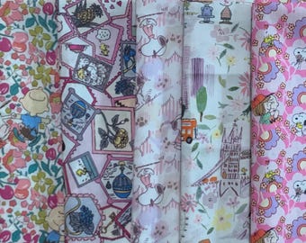 Può includere: Una collezione di rotoli di tessuto fantasia. I disegni includono motivi floreali, personaggi dei cartoni animati e motivi architettonici in rosa, bianco e altri colori. I tessuti sono probabilmente in cotone o simili, per cucito o patchwork.