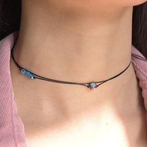 May include: A delicate black choker necklace with two small glass beads. One bead is blue with white speckles, and the other is a multi-colored geometric shape.