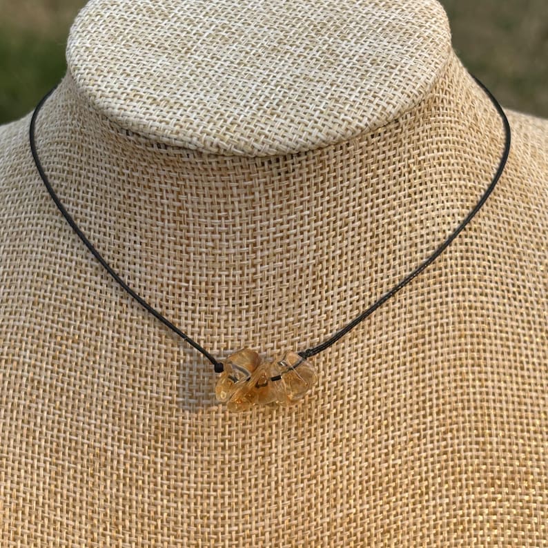 May include: A simple necklace with a brown cord and a golden brown crystal pendant.