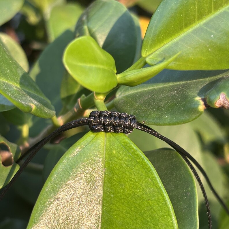May include: Close-up of a black cord with a knot tied in it. The cord is resting on a green leaf.