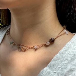 May include: A brown leather cord necklace with multiple small stones in shades of brown, white, and green.