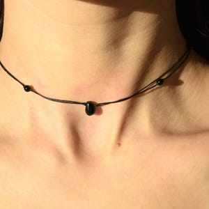 May include: A simple black choker necklace with a single black teardrop-shaped pendant and two small black beads.