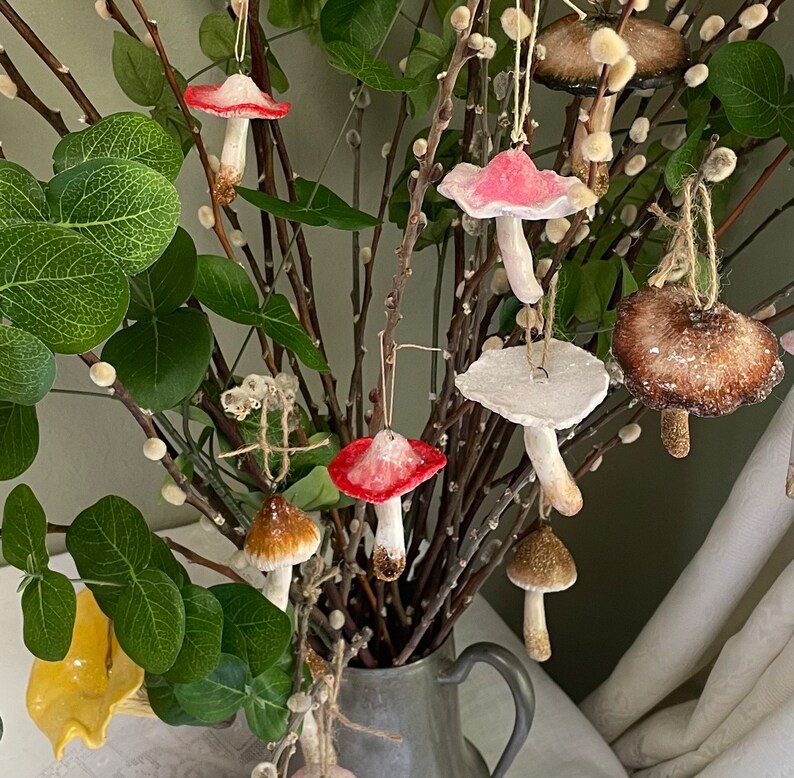 clay glittery mushroom ornament assortment, hanging from branches , grey background