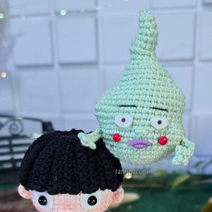 Könnte beinhalten: Gehäkelte Amigurumi-Figuren von zwei Anime-Charakteren. Eine Figur hat schwarze Haare und eine schwarze Uniform mit goldenen Knöpfen. Die andere ist eine hellgrüne, tropfenförmige Figur mit einem Gesicht. Der Text "ramyugurumi" ist sichtbar.