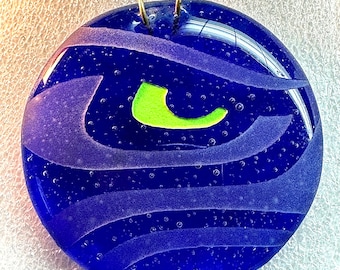 May include: A blue glass ornament with a green and white design. The ornament has a textured surface and a gold hanger.