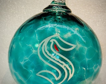 May include: A teal blue glass Christmas ornament with a white 'S' etched on the front. The ornament has a clear glass loop for hanging.