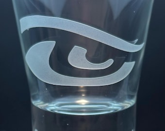 May include: Clear shot glass with a frosted eye-shaped design. The text "Super Bowl LX 2020" is etched at the base. The glass is cylindrical and appears to be empty.
