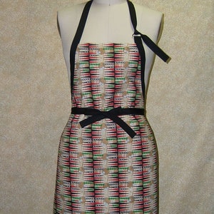 May include: A black and white patterned apron with red and green accents. The apron has a black ribbon tie and is made of a fabric with a geometric design.