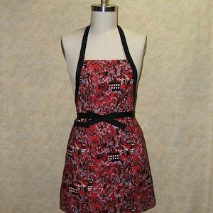 May include: A red and black apron with a city skyline pattern. The apron has a black ribbon tie.