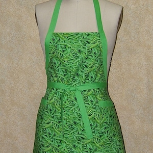 May include: A green apron with a pattern of green peas. The apron has a green tie and two pockets.
