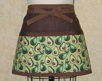 Pode incluir: Um avental marrom e verde com um bolso e uma gravata. O avental tem um padrão de abacates em um fundo verde.