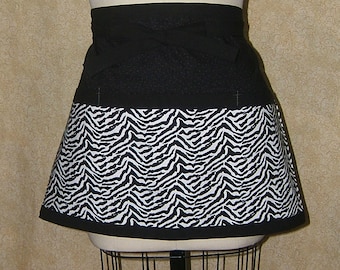 Pode incluir: Um avental com estampa de zebra em preto e branco, com cós e acabamento em preto. O avental é exibido em um manequim. A estampa de zebra está na metade inferior.