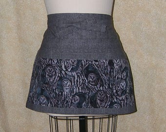 Pode incluir: Uma saia cinza com um padrão de coruja. A saia apresenta uma cintura cinza lisa e uma seção inferior com um padrão repetido de corujas em um ambiente florestal. O tecido tem uma aparência texturizada.