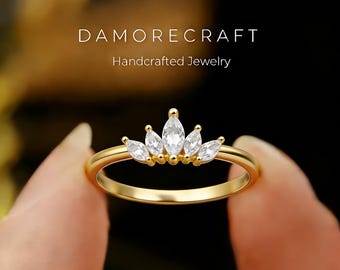 May include: A gold ring with a crown design, featuring five marquise-cut white gemstones. The ring is held by a person's hand. The text "DAMORECRAFT Handcrafted Jewelry" is visible in the background.