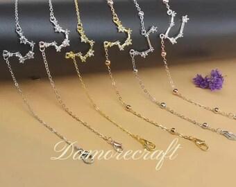 Op de afbeelding: Een set van zeven zilveren en gouden kettingen met stervormige hangers. De kettingen zijn van verschillende lengtes en hebben kleine kralen langs de ketting.