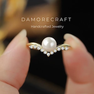 Op de afbeelding: Een gouden ring met een enkele parel en een rij kleine diamanten in een V-vorm. DAMORECRAFT Handgemaakt juweel.