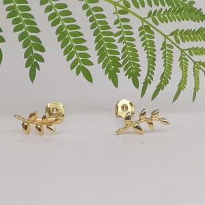 May include: A pair of gold leaf earrings. Each earring features a delicate branch with multiple leaves.