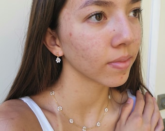 Op de afbeelding: Een gouden kettingketting en armband met kleine witte bloemenbedels. De ketting heeft zeven bedels en de armband vijf.