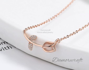 May include: A delicate rose gold necklace with a rosebud pendant featuring a white stone and sparkling clear stones. The chain is a simple, linked design. "Damorecraft Handcrafted Jewelry" is printed on the white background.