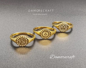 Op de afbeelding: Drie gouden zegelringen met verschillende hemelmotieven. De ringen tonen een zon, een maan en een gezicht met gesloten ogen. De ringen liggen op een grijs oppervlak met de tekst "Damorecraft Handmade Jewelry" boven de ringen en "Damorecraft" onder de ringen.