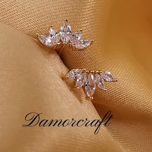 May include: Two gold rings with a marquise-shaped diamond design. The rings are on a gold fabric background.