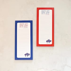 May include: Two rectangular notepads, one blue and one red, with white lined paper. Each notepad features the text "HEY-EY EY-EY" and a buffalo graphic in blue and purple. The notepads are designed for jotting down notes.