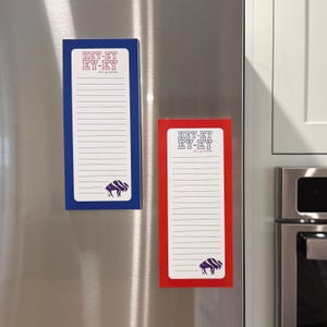 May include: Two rectangular magnetic notepads are displayed on a stainless steel refrigerator. One notepad has a blue border, and the other has a red border. Both have the text "HEY-EY EY-EY let's go buffalo" and a buffalo graphic.
