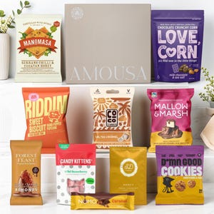 May include: A gift box labelled AMOUSA surrounded by various snack packets including Manomasa tortilla chips, Love Corn, Riddim popcorn, Coco Cubes, Mallow & Marsh, Forest Feast almonds, Candy Kittens, SD Honey, Nomo chocolate, and D*mn Good Cookies.