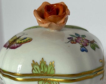 May include: A white porcelain trinket box with a green and gold floral design. The lid features a three-dimensional orange rose and a butterfly.