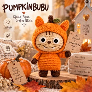 Könnte beinhalten: Eine Häkelpuppe mit einer orangefarbenen Kürbis-Kapuze mit Katzenohren, die ein Holzschild mit der Aufschrift 'Be yourself it's pumpkinbubu time!' hält. Die Puppe hat ein beiges Gesicht, schwarze Augen und braune Pfoten auf einer Holzscheibe.