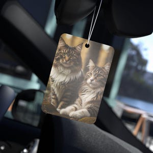 Könnte beinhalten: Zwei braune Tabby-Katzen mit weißen Markierungen sitzen zusammen in einer Waldlandschaft. Die Katze links schaut in die Kamera, während die Katze rechts zur Seite schaut. Beide Katzen sitzen auf einem Bett aus Blättern.