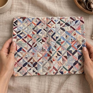May include: A rectangular quilted fabric piece featuring a patchwork design composed of numerous small, multi-colored triangular fabric scraps in various patterns, including stripes, florals, and solid colors, stitched together in a grid pattern.