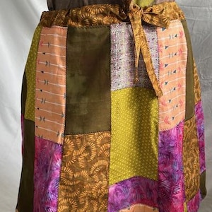 May include: A patchwork skirt with a variety of colorful fabric squares. The skirt features shades of green, pink, orange, and brown. The waistband has a drawstring tie. The skirt is a unique, handmade piece.