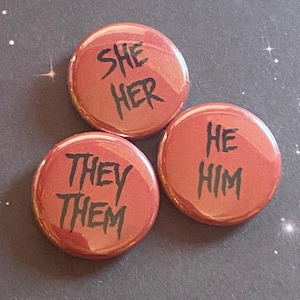 May include: Three red round buttons with black text. The first button says "She Her", the second button says "He Him", and the third button says "They Them".