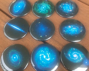 Puede incluir: Diez botones redondos azules y verdes con imágenes de galaxias y nebulosas.