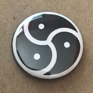 Könnte beinhalten: Ein schwarzer und weißer Knopf mit einem Triquetra-Symbol. Das Symbol ist ein stilisierter Knoten aus drei ineinandergreifenden Kreisen.