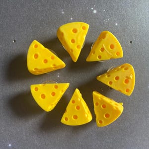 May include: Seven yellow cheese-shaped buttons with holes. The buttons are arranged in a circle on a gray surface.