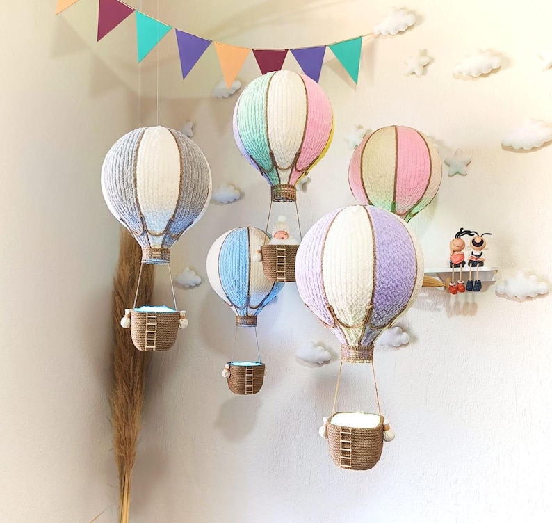 May include: A set of five colourful hot air balloons with baskets hanging from them. The balloons are made of yarn and are decorated with stripes and dots. The baskets are made of woven material and have a light inside them.